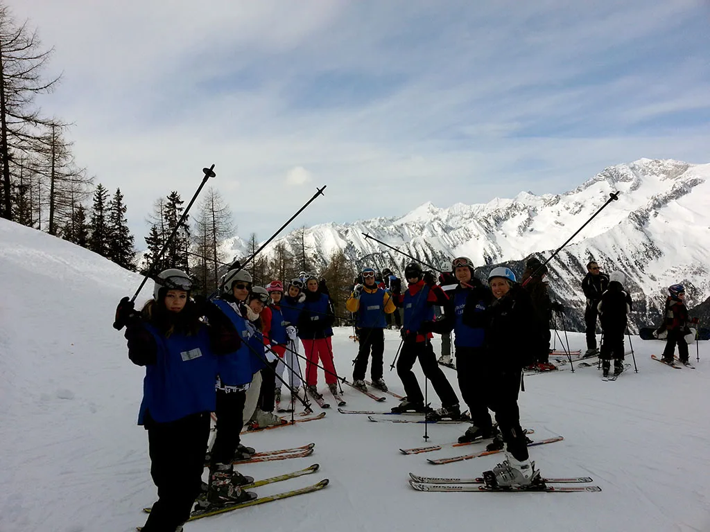 Skigruppe steht am Pistenrand vor der Bergkulisse.